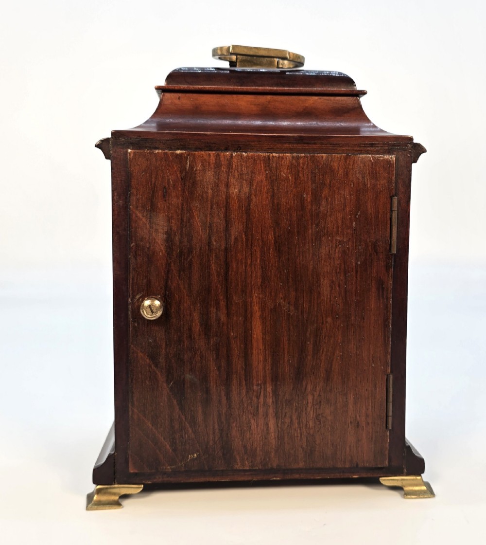 A miniature George II style wooden bracket clock featuring a caddy top with brass handle, engraved silvered dial with Roman numerals, and brass feet. View VI