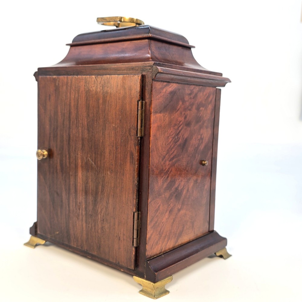 A miniature George II style wooden bracket clock featuring a caddy top with brass handle, engraved silvered dial with Roman numerals, and brass feet. View VII