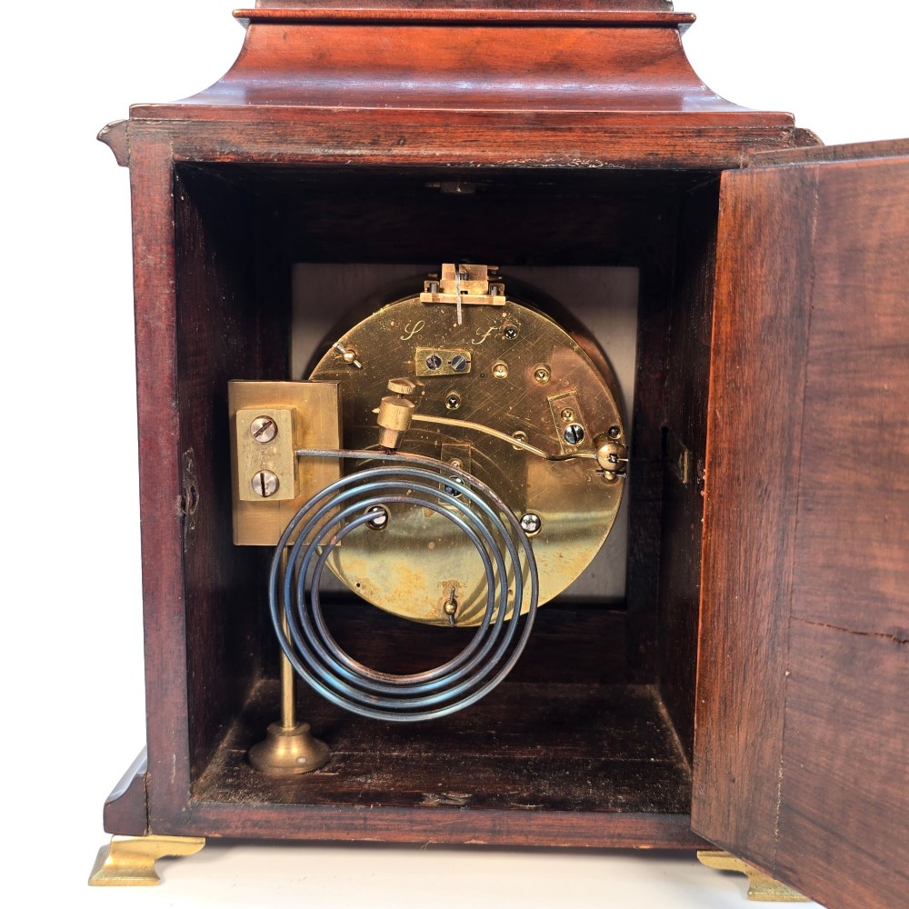 A miniature George II style wooden bracket clock featuring a caddy top with brass handle, engraved silvered dial with Roman numerals, and brass feet. View VIII