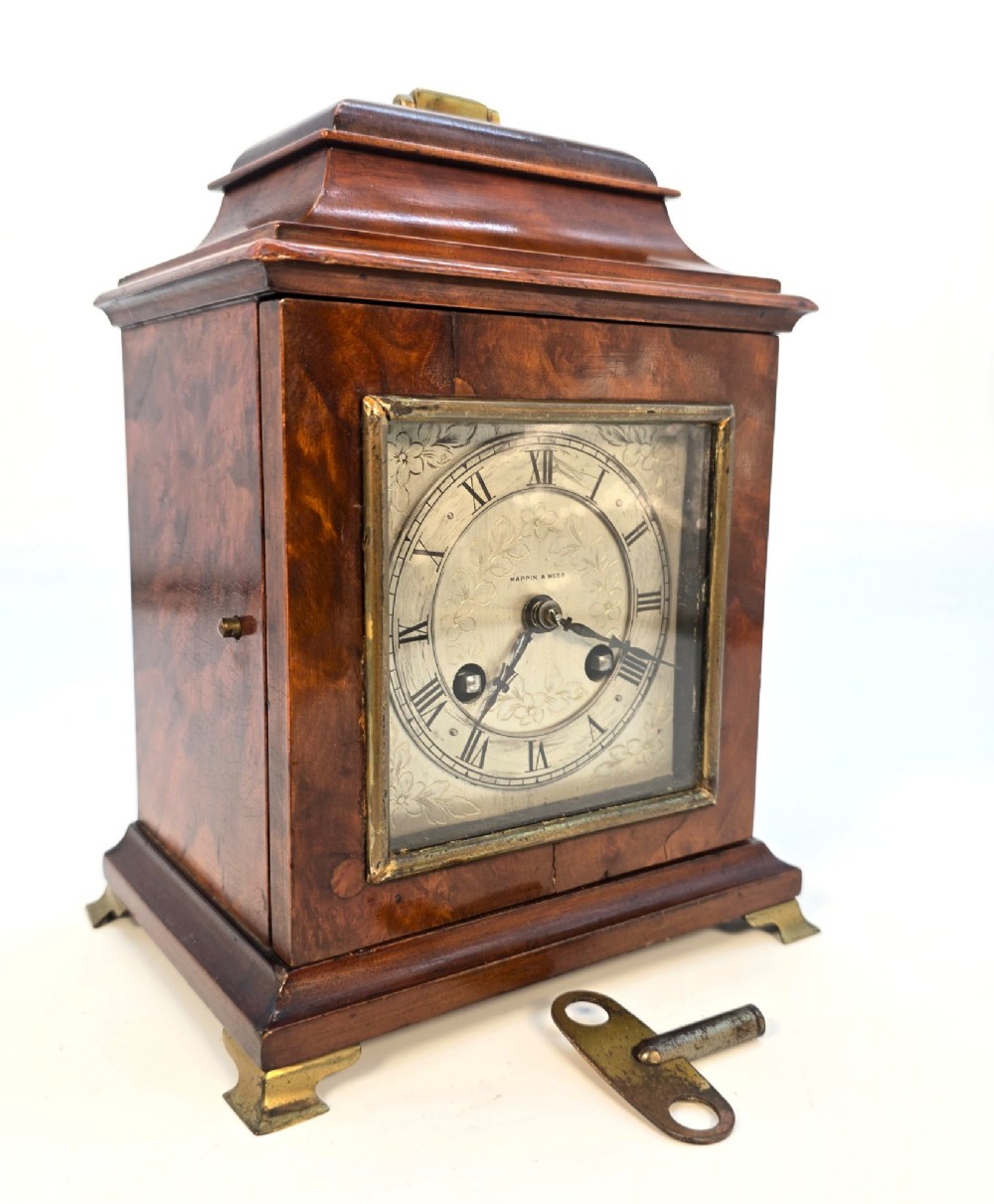 A miniature George II style wooden bracket clock featuring a caddy top with brass handle, engraved silvered dial with Roman numerals, and brass feet. View X