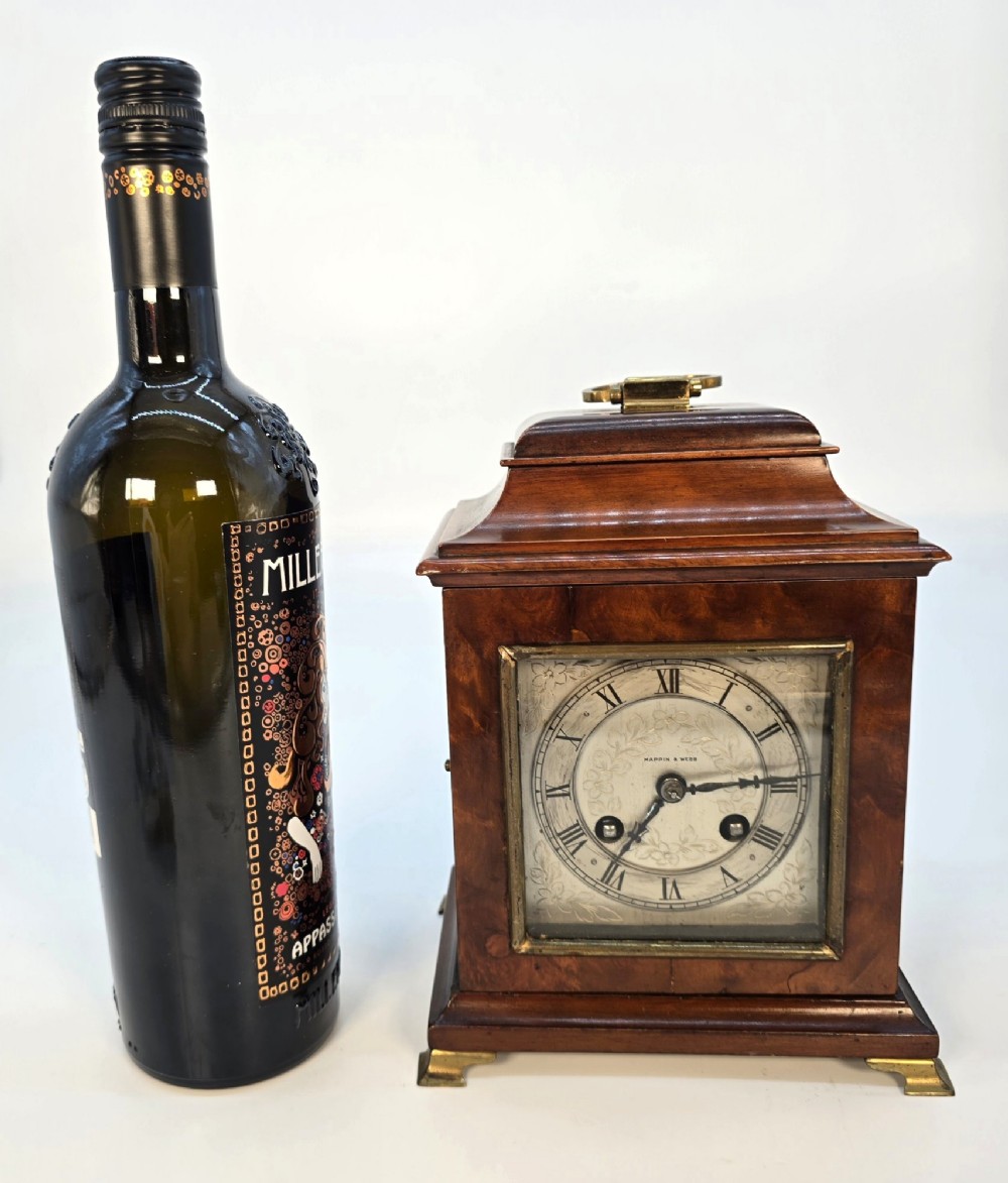 A miniature George II style wooden bracket clock featuring a caddy top with brass handle, engraved silvered dial with Roman numerals, and brass feet. View XII