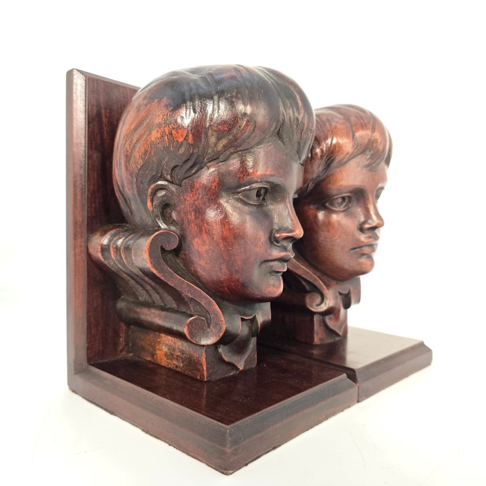A pair of carved mahogany bookends depicting the profile busts of choir boys mounted on L-shaped wooden bases. View V