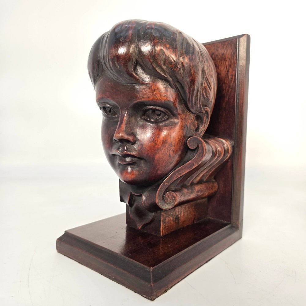 A pair of carved mahogany bookends depicting the profile busts of choir boys mounted on L-shaped wooden bases. View IX