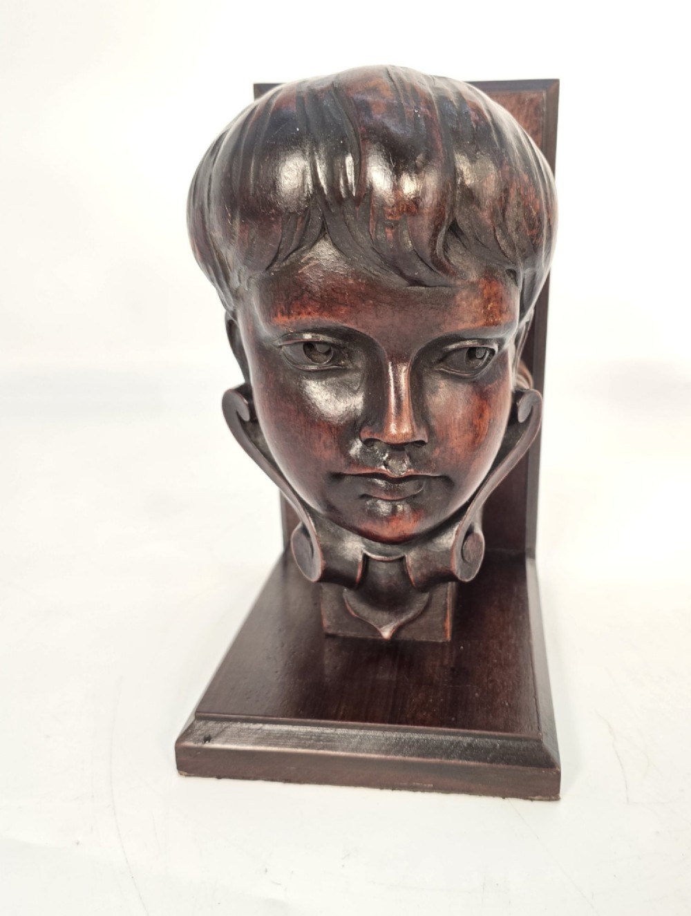 A pair of carved mahogany bookends depicting the profile busts of choir boys mounted on L-shaped wooden bases. View X