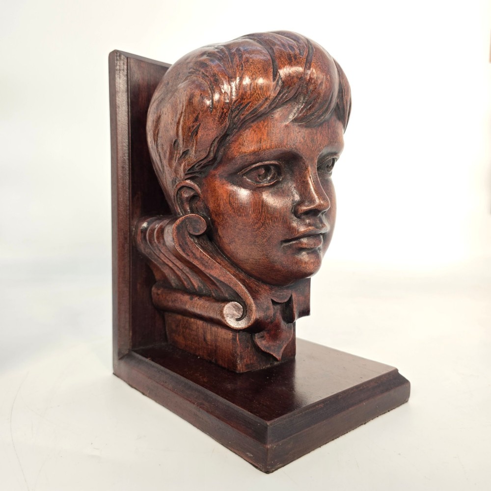 A pair of carved mahogany bookends depicting the profile busts of choir boys mounted on L-shaped wooden bases. View XIII