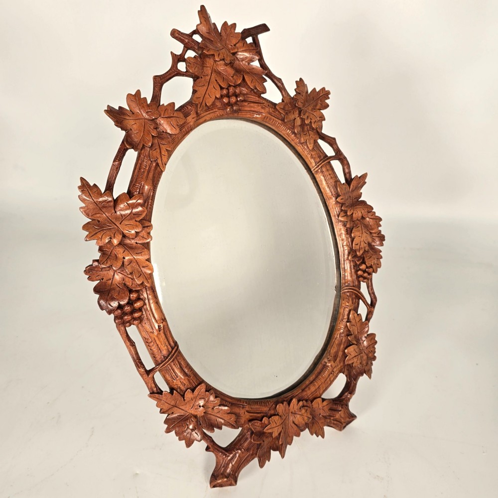 A late nineteenth-century Swiss carved lime wood oval table mirror surrounded by relief carvings of grapevine leaves and grapes.