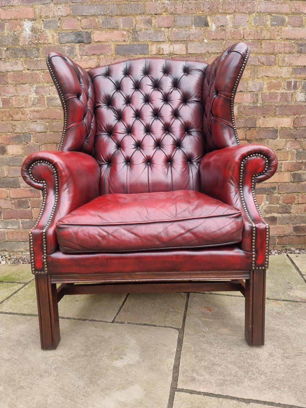 A George III style wingback armchair upholstered in deep buttoned burgundy red leather with brass stud detailing and square mahogany legs. View II