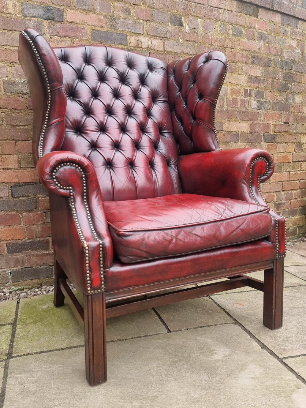 A George III style wingback armchair upholstered in deep buttoned burgundy red leather with brass stud detailing and square mahogany legs. View III