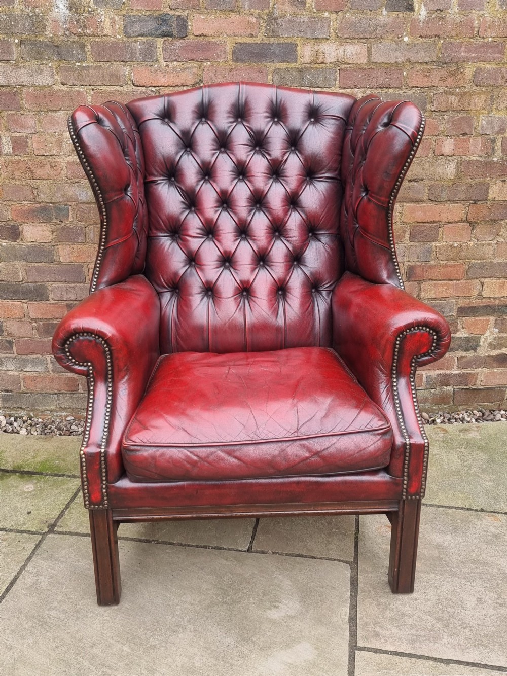 A George III style wingback armchair upholstered in deep buttoned burgundy red leather with brass stud detailing and square mahogany legs. View IV