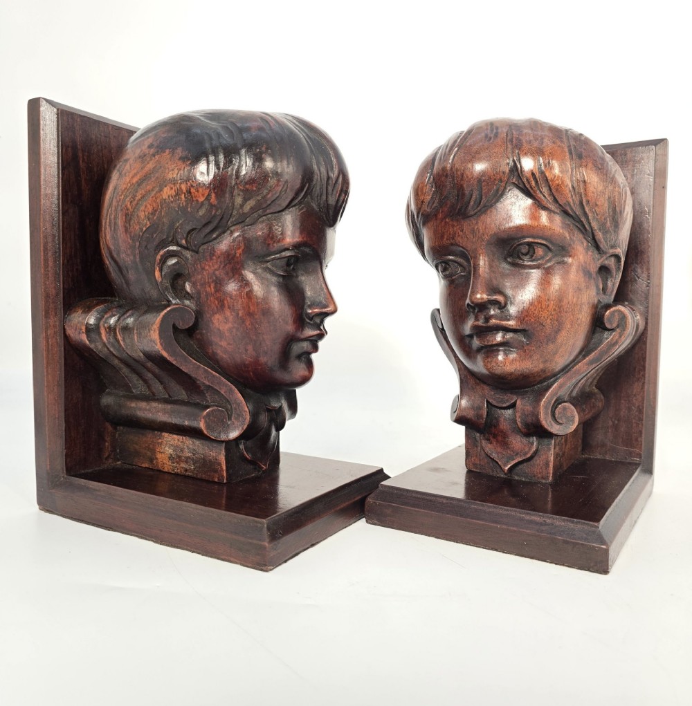 A pair of carved mahogany bookends featuring profile busts of children mounted on L-shaped wooden bases. View VII