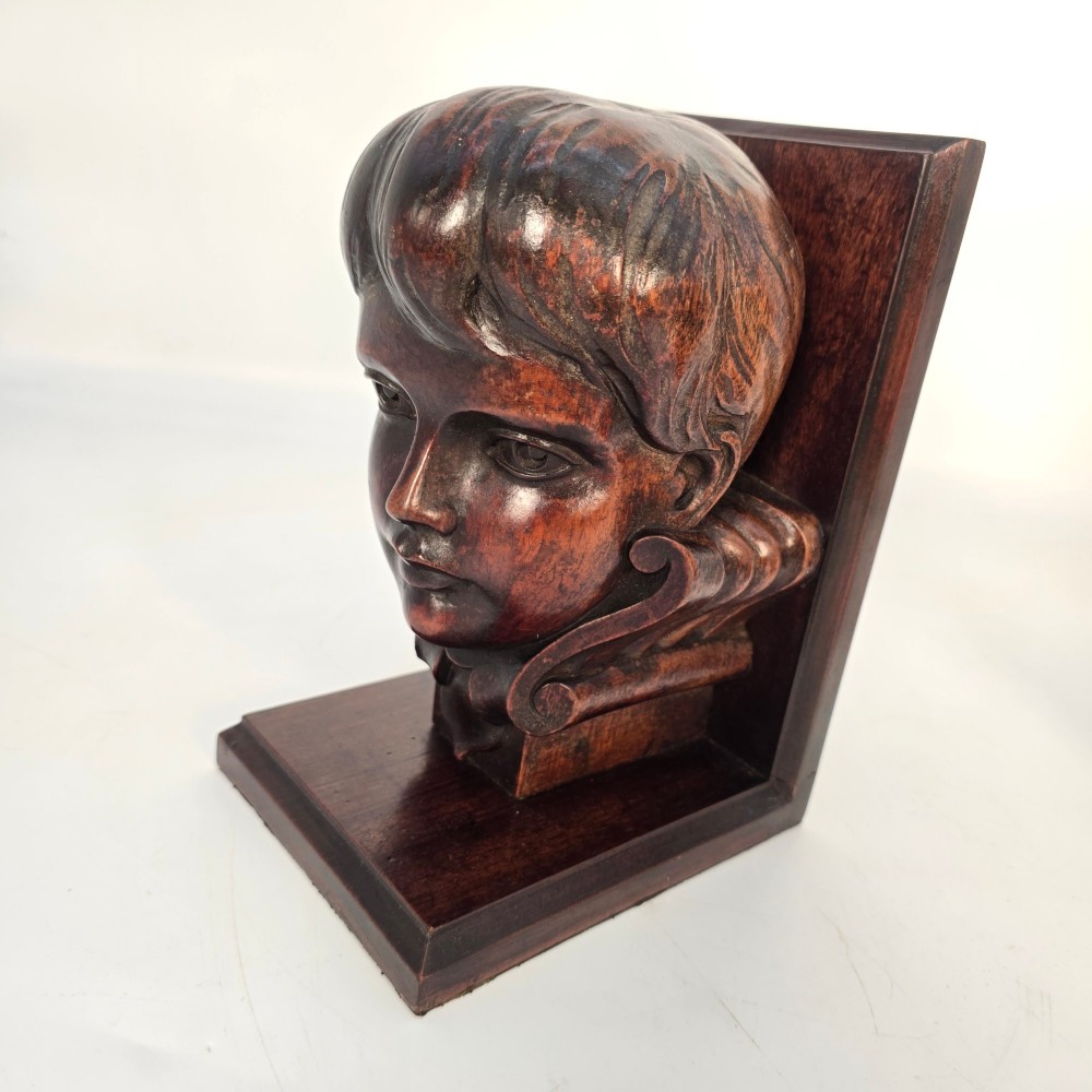 A pair of carved mahogany bookends featuring profile busts of children mounted on L-shaped wooden bases. View XI