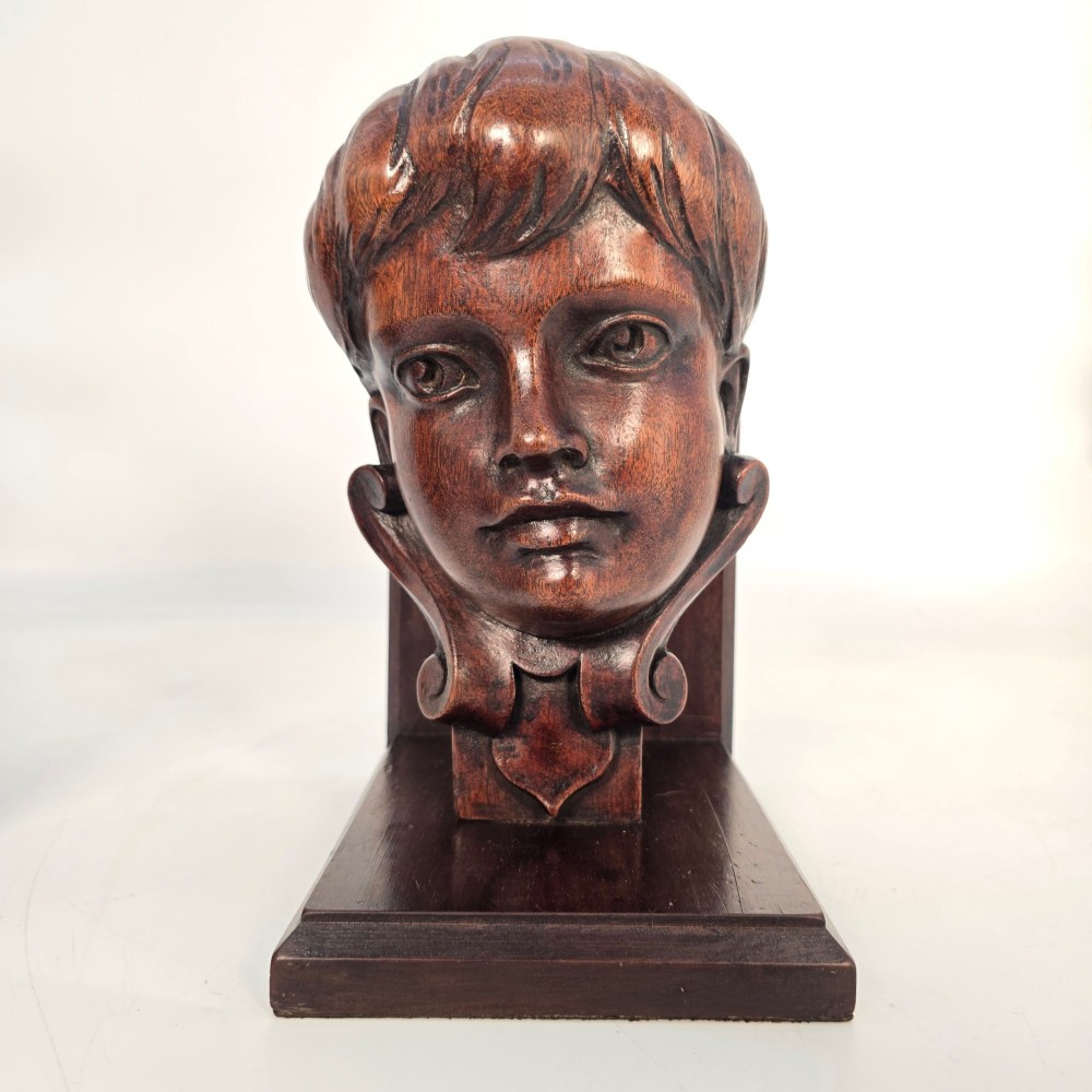 A pair of carved mahogany bookends featuring profile busts of children mounted on L-shaped wooden bases. View XII