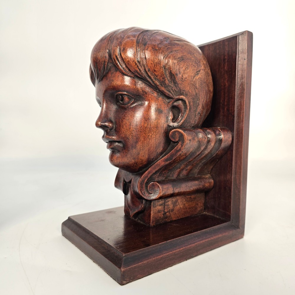 A pair of carved mahogany bookends featuring profile busts of children mounted on L-shaped wooden bases. View XIV