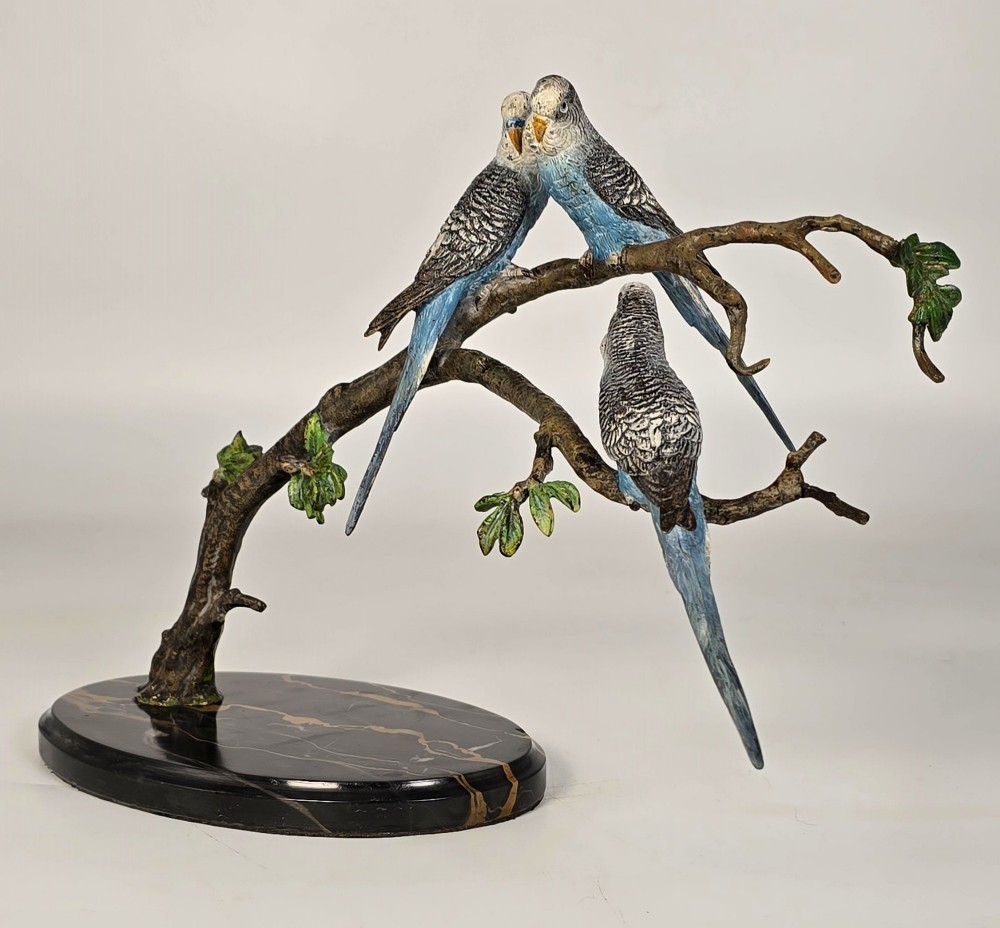 A cold-painted bronze sculpture featuring three blue and grey budgerigars perched on a leafy bronze branch, mounted on an oval dark marble base. View II