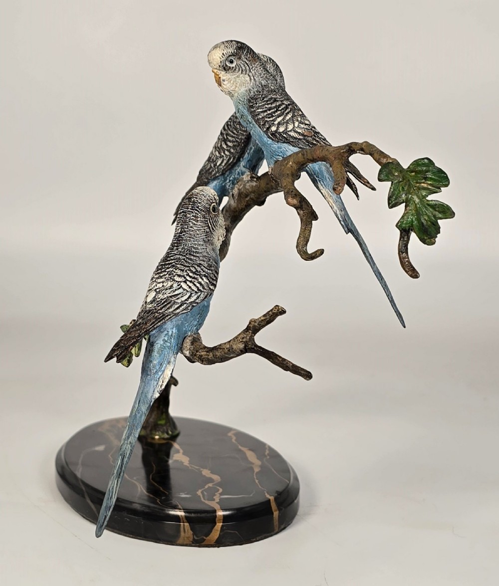A cold-painted bronze sculpture featuring three blue and grey budgerigars perched on a leafy bronze branch, mounted on an oval dark marble base. View III