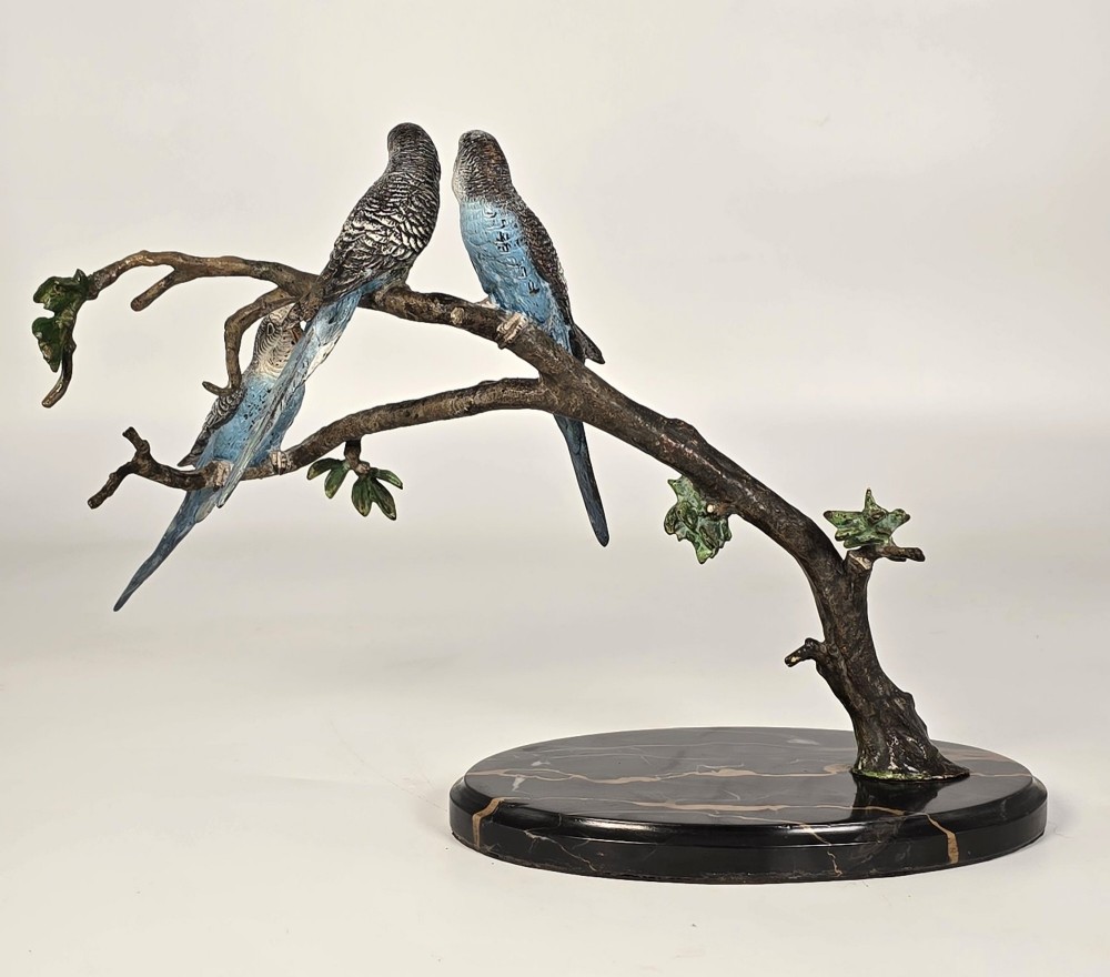 A cold-painted bronze sculpture featuring three blue and grey budgerigars perched on a leafy bronze branch, mounted on an oval dark marble base. View V
