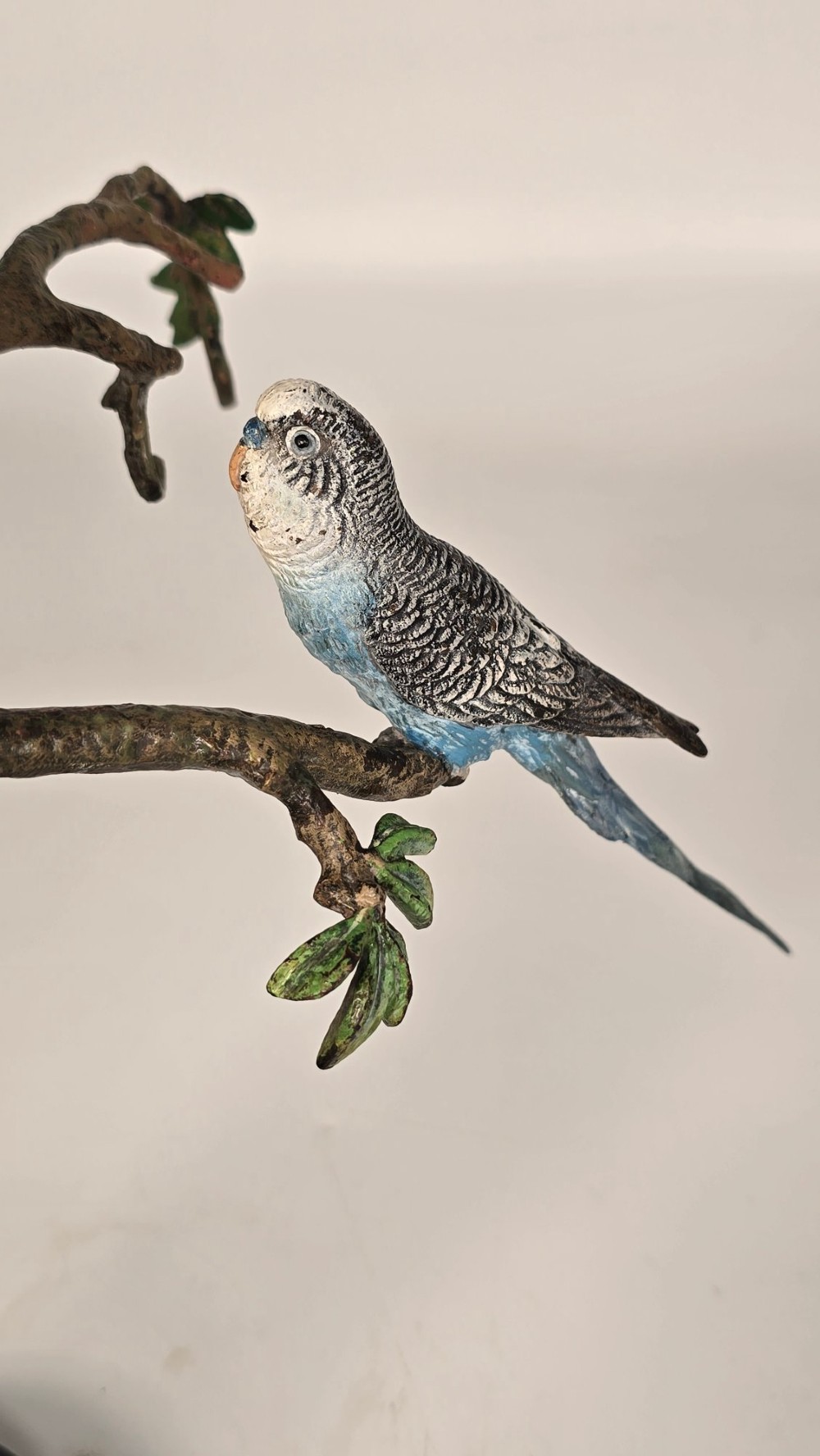 A cold-painted bronze sculpture featuring three blue and grey budgerigars perched on a leafy bronze branch, mounted on an oval dark marble base. View VI