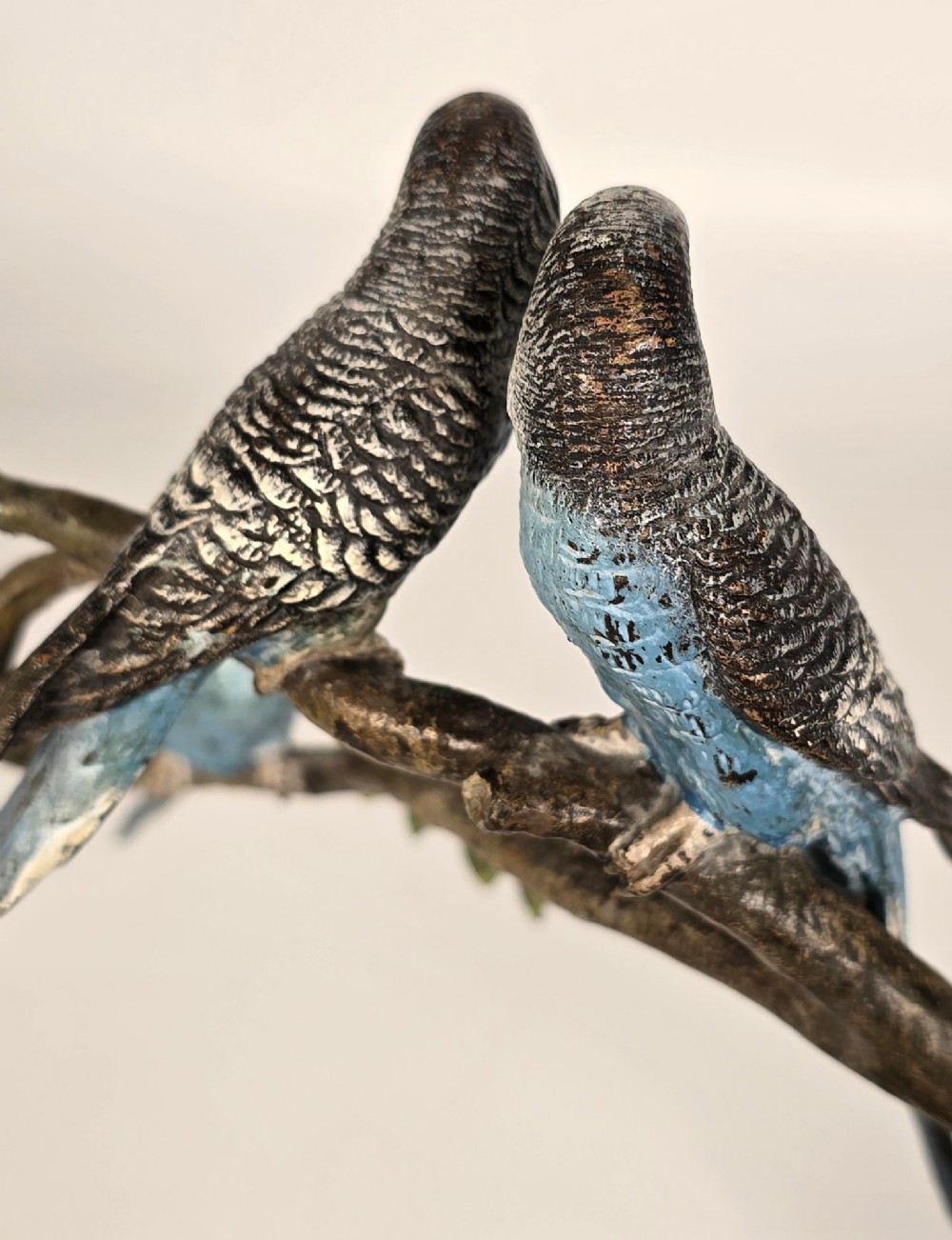 A cold-painted bronze sculpture featuring three blue and grey budgerigars perched on a leafy bronze branch, mounted on an oval dark marble base. View IX