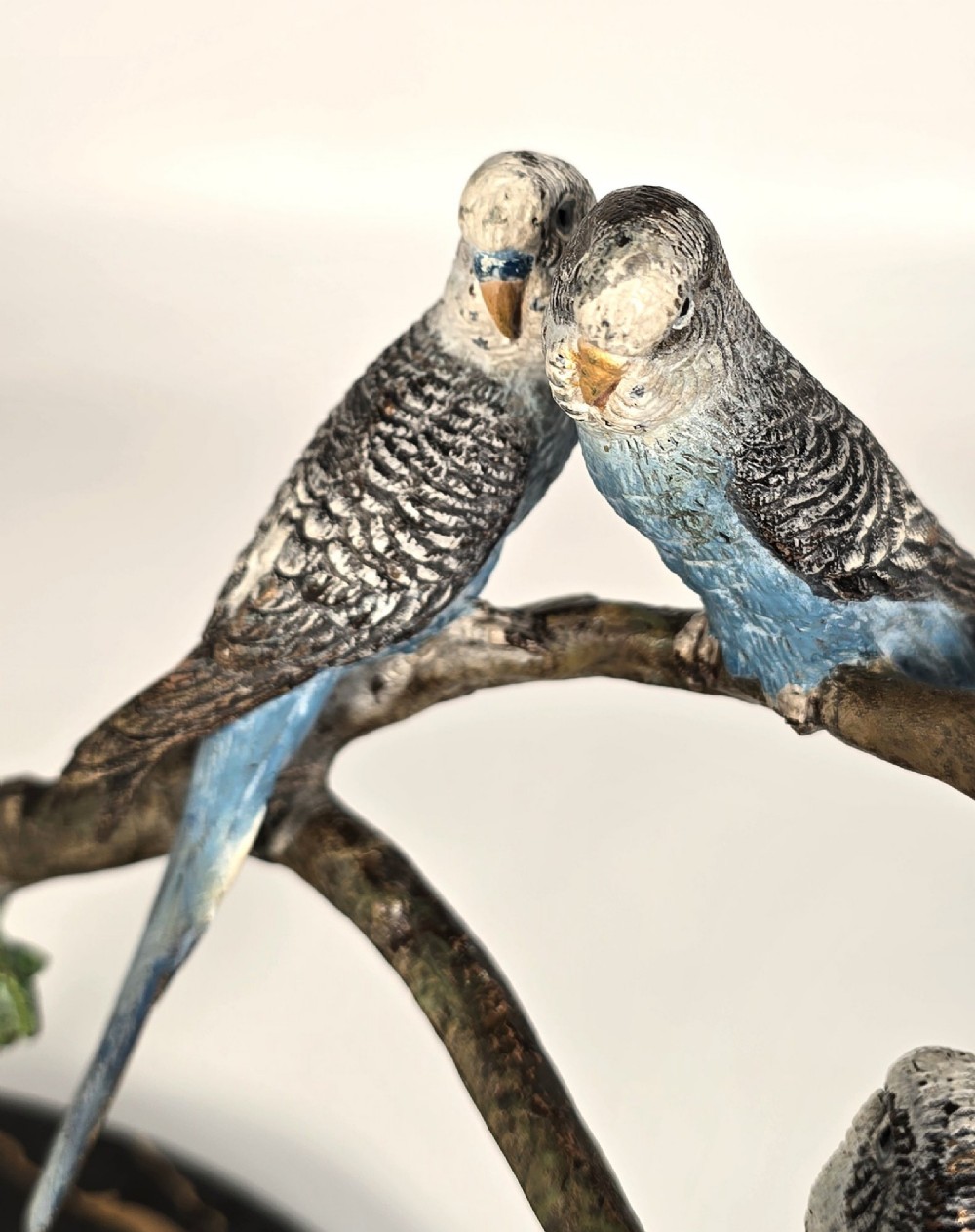 A cold-painted bronze sculpture featuring three blue and grey budgerigars perched on a leafy bronze branch, mounted on an oval dark marble base. View XI