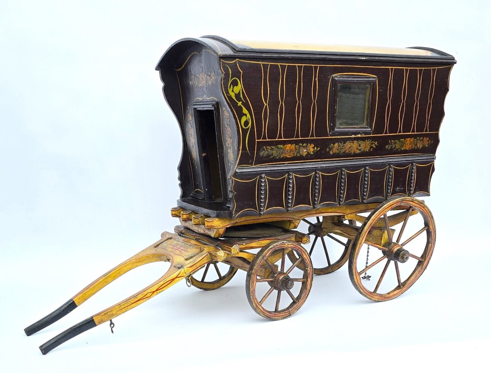 Hand-painted Edwardian wooden scale model of a Romani vardo caravan in dark brown and yellow with floral motifs and spoked wheels.