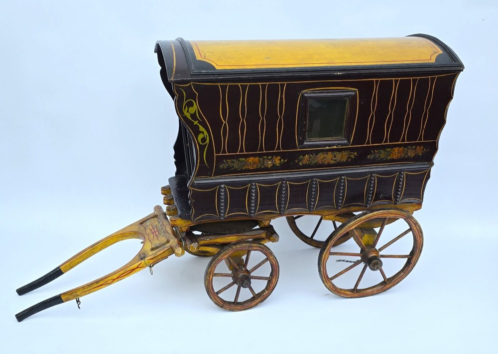 Hand-painted Edwardian wooden scale model of a Romani vardo caravan in dark brown and yellow with floral motifs and spoked wheels. View II
