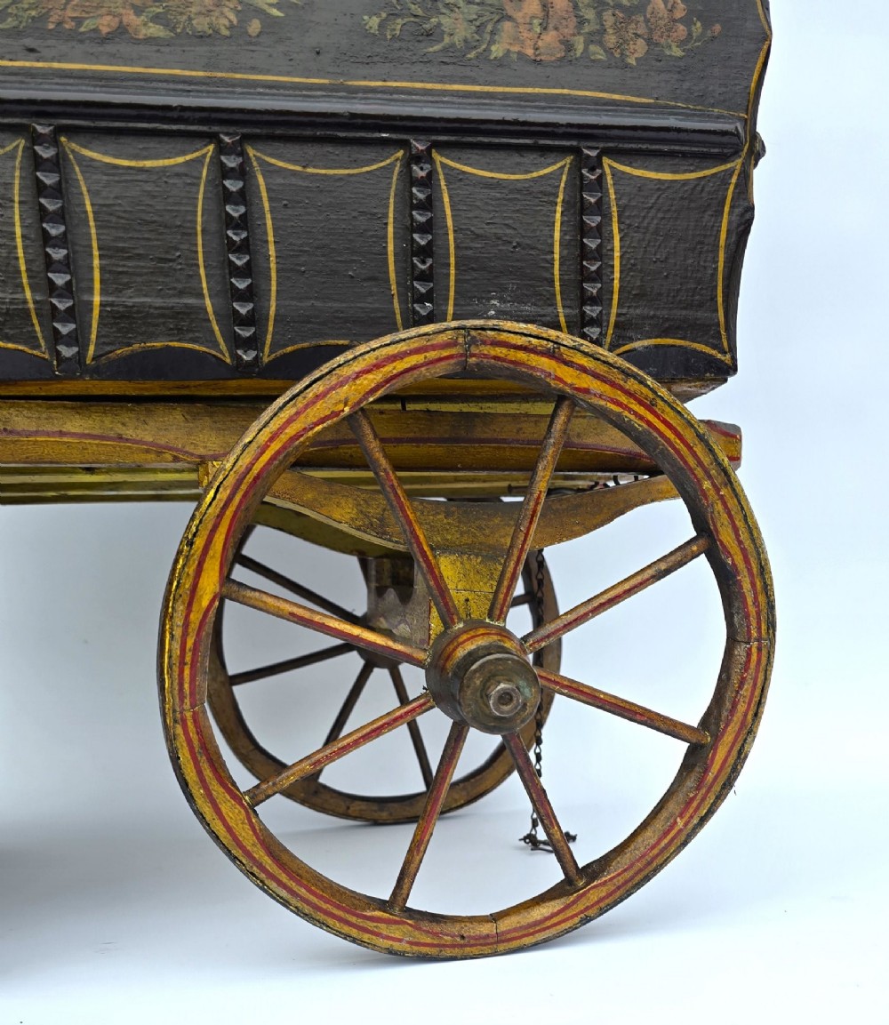Hand-painted Edwardian wooden scale model of a Romani vardo caravan in dark brown and yellow with floral motifs and spoked wheels. View III