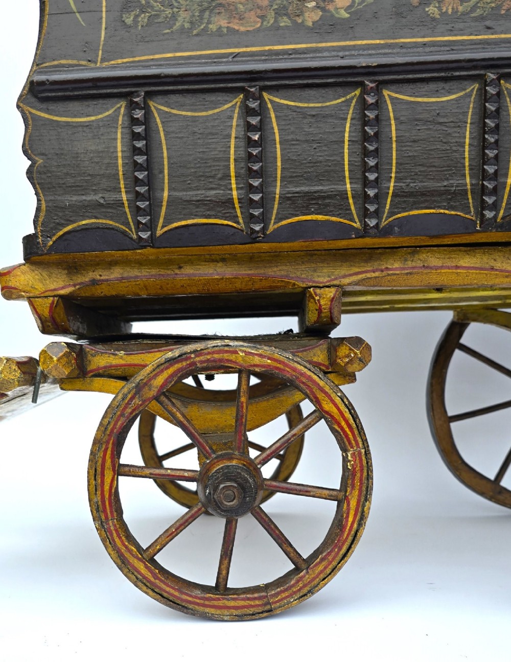Hand-painted Edwardian wooden scale model of a Romani vardo caravan in dark brown and yellow with floral motifs and spoked wheels. View IV