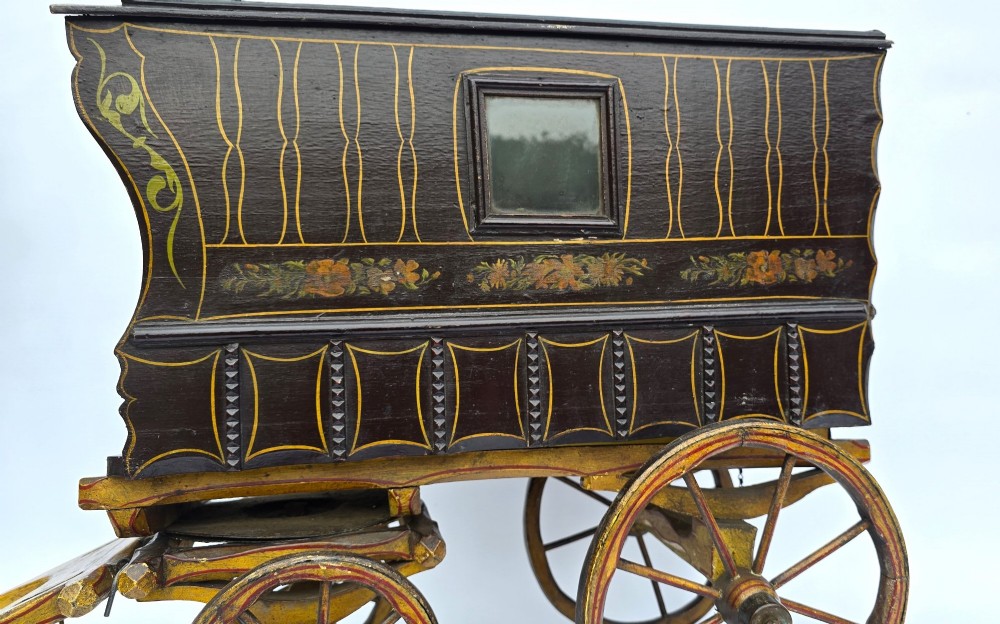 Hand-painted Edwardian wooden scale model of a Romani vardo caravan in dark brown and yellow with floral motifs and spoked wheels. View V