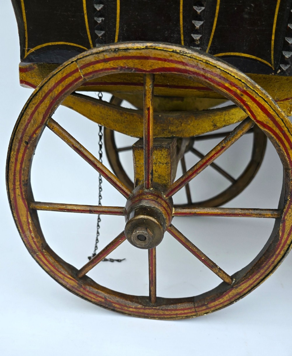 Hand-painted Edwardian wooden scale model of a Romani vardo caravan in dark brown and yellow with floral motifs and spoked wheels. View VI