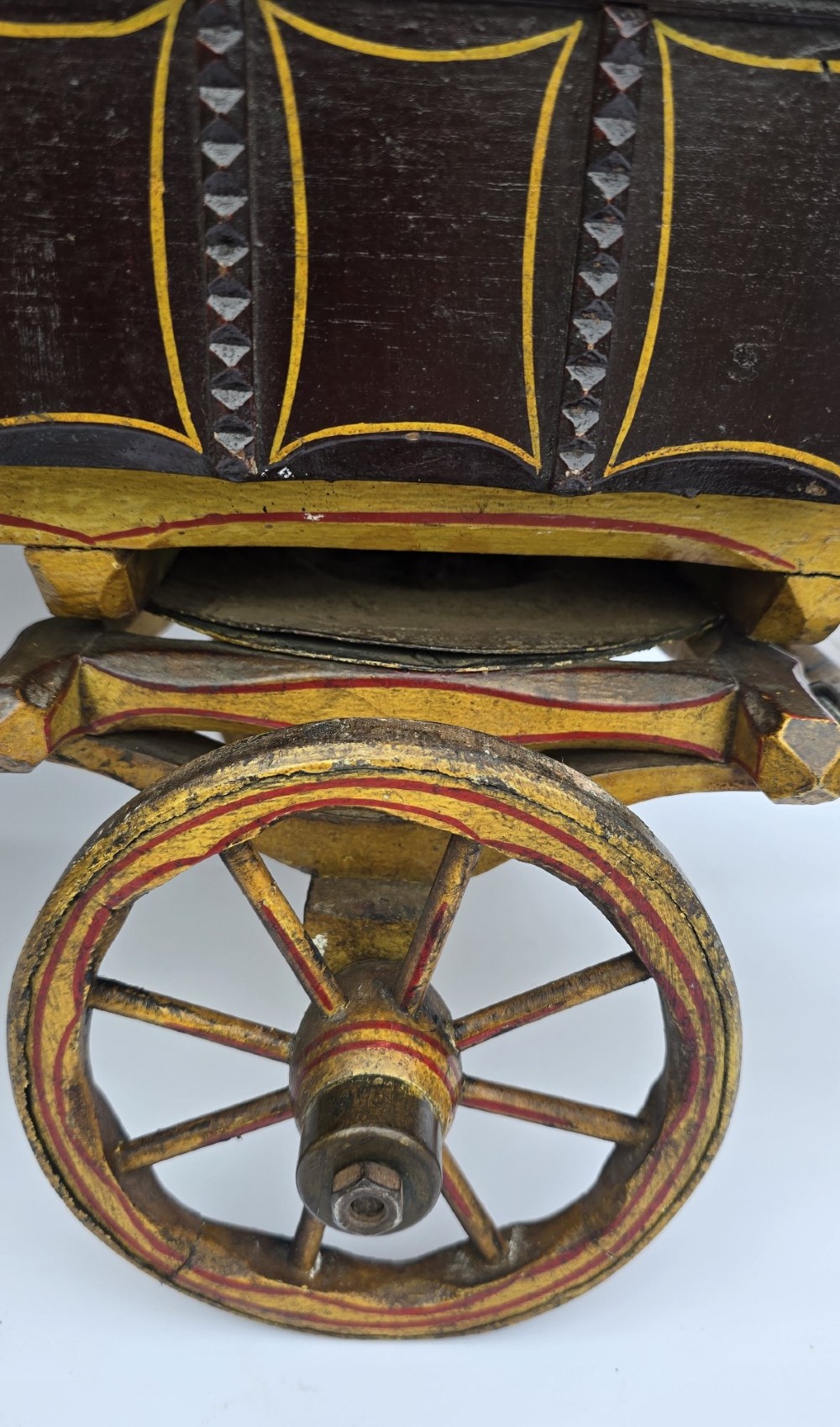 Hand-painted Edwardian wooden scale model of a Romani vardo caravan in dark brown and yellow with floral motifs and spoked wheels. View VII