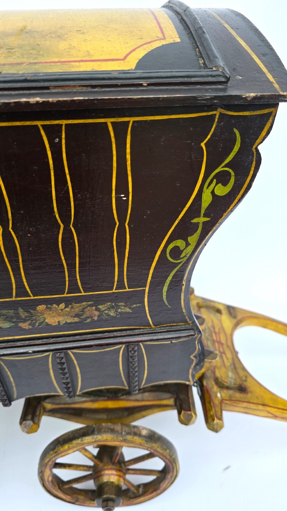 Hand-painted Edwardian wooden scale model of a Romani vardo caravan in dark brown and yellow with floral motifs and spoked wheels. View X