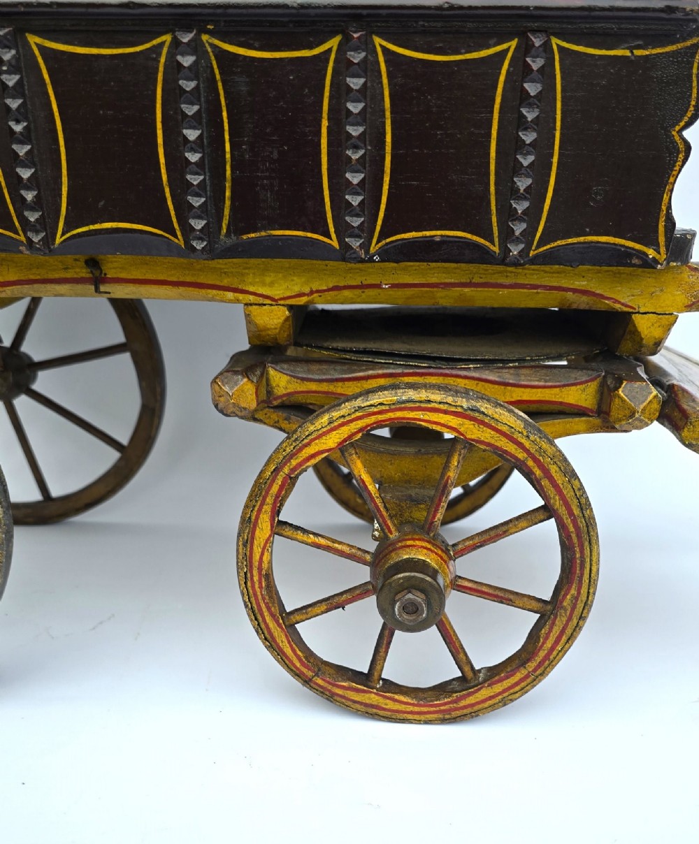 Hand-painted Edwardian wooden scale model of a Romani vardo caravan in dark brown and yellow with floral motifs and spoked wheels. View XI