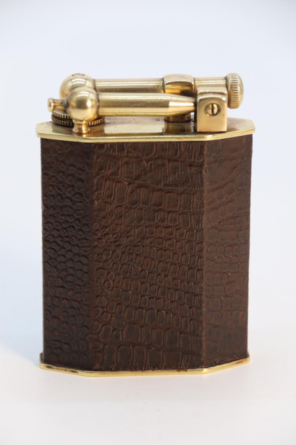 An Art Deco French table lighter featuring a textured brown leather-wrapped faceted body and a polished brass lift-arm ignition mechanism.