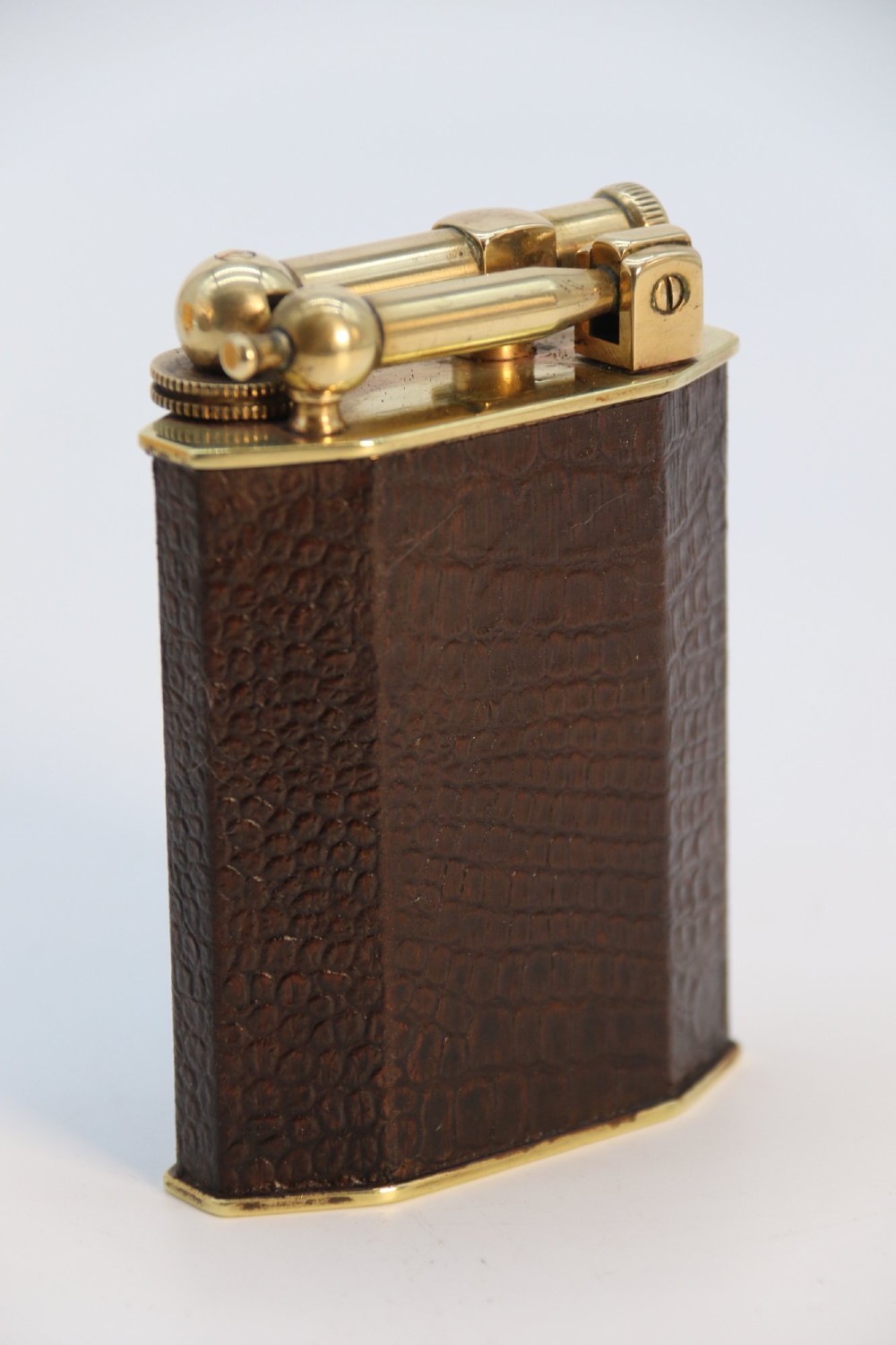 An Art Deco French table lighter featuring a textured brown leather-wrapped faceted body and a polished brass lift-arm ignition mechanism. View II