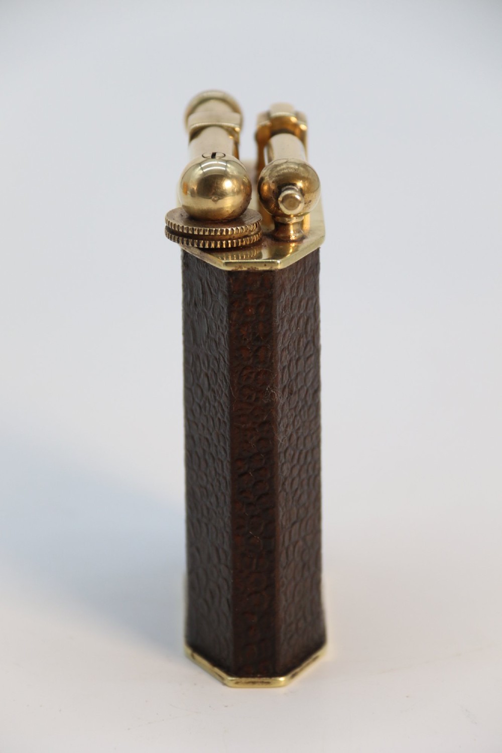 An Art Deco French table lighter featuring a textured brown leather-wrapped faceted body and a polished brass lift-arm ignition mechanism. View III
