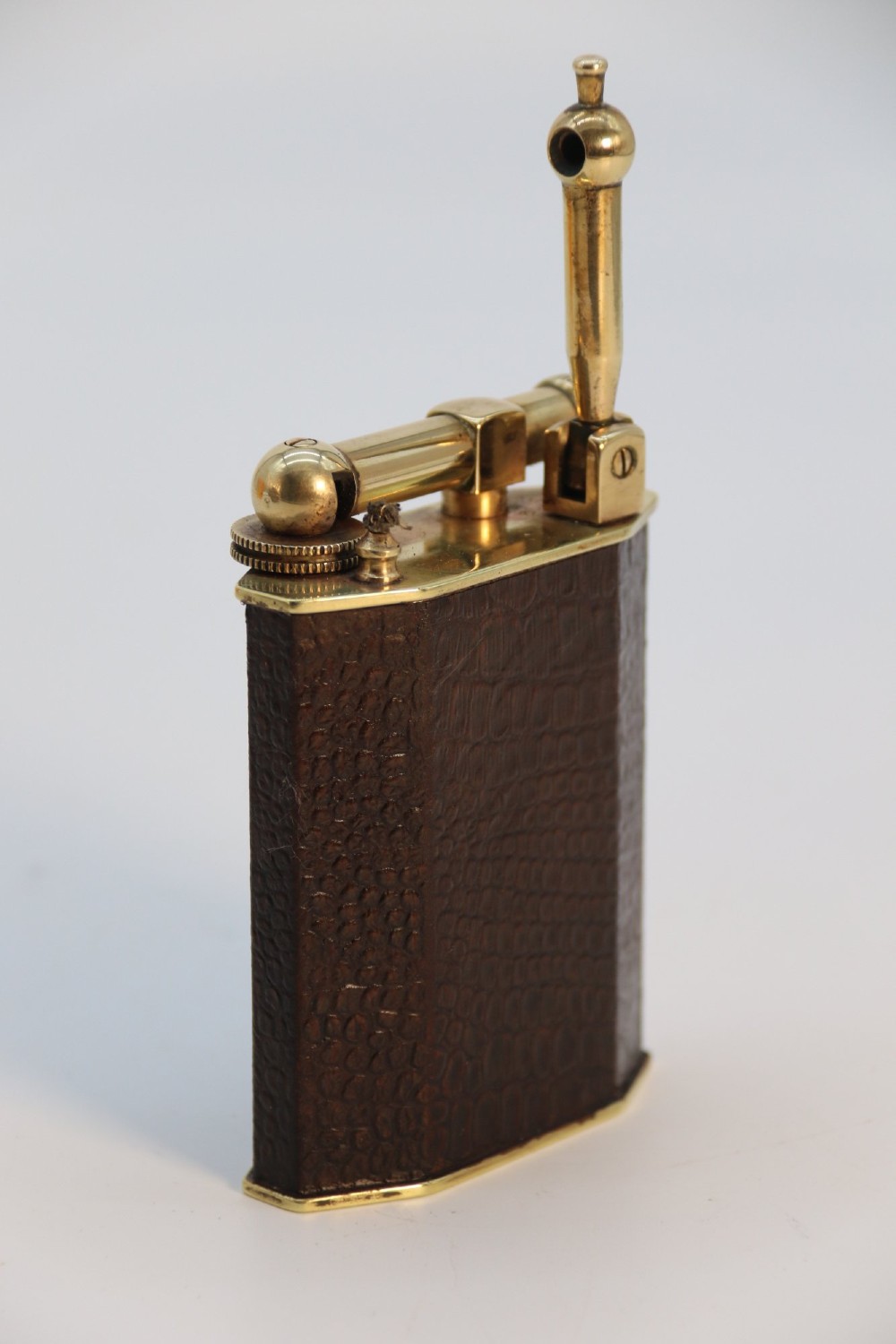 An Art Deco French table lighter featuring a textured brown leather-wrapped faceted body and a polished brass lift-arm ignition mechanism. View VI