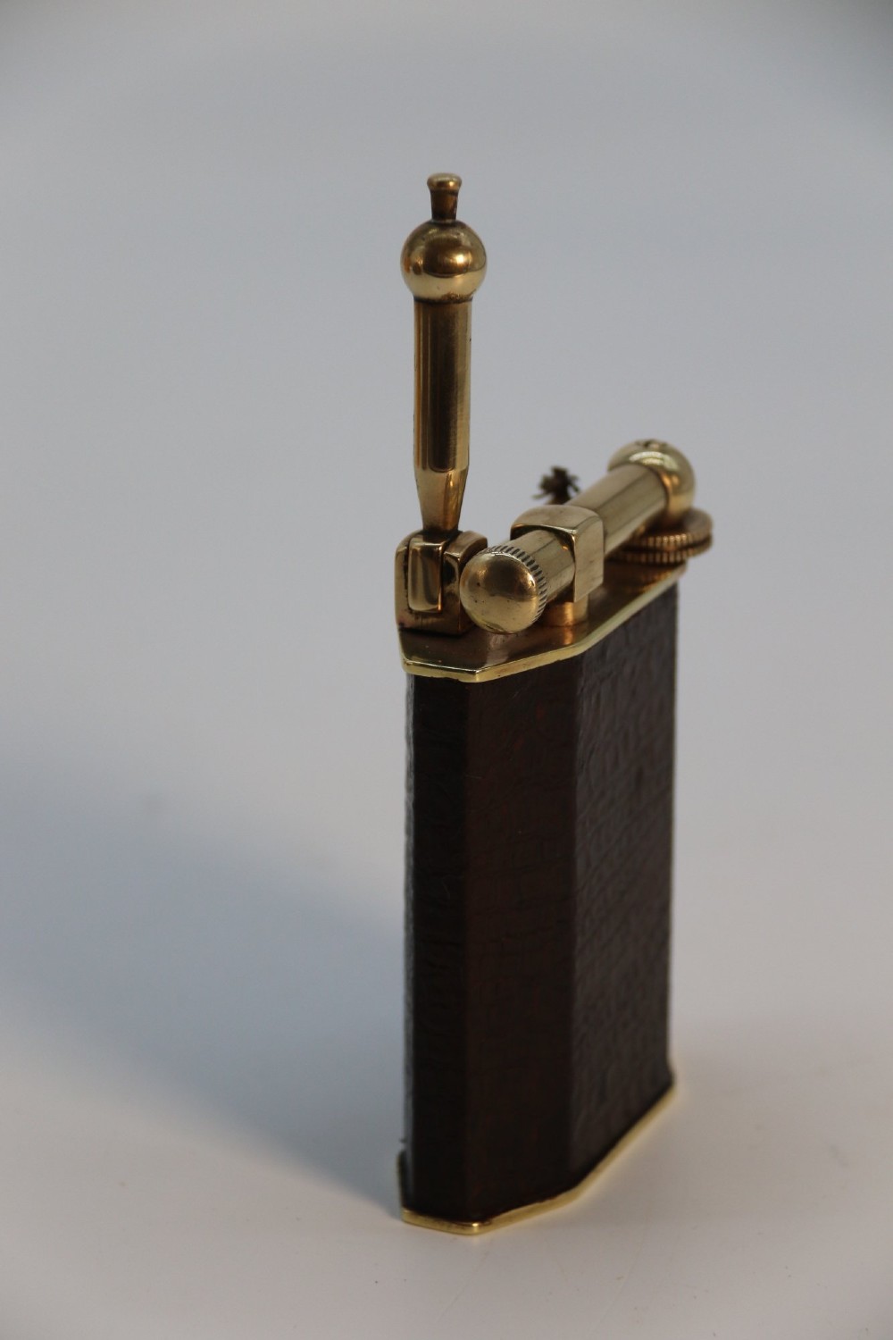 An Art Deco French table lighter featuring a textured brown leather-wrapped faceted body and a polished brass lift-arm ignition mechanism. View VIII