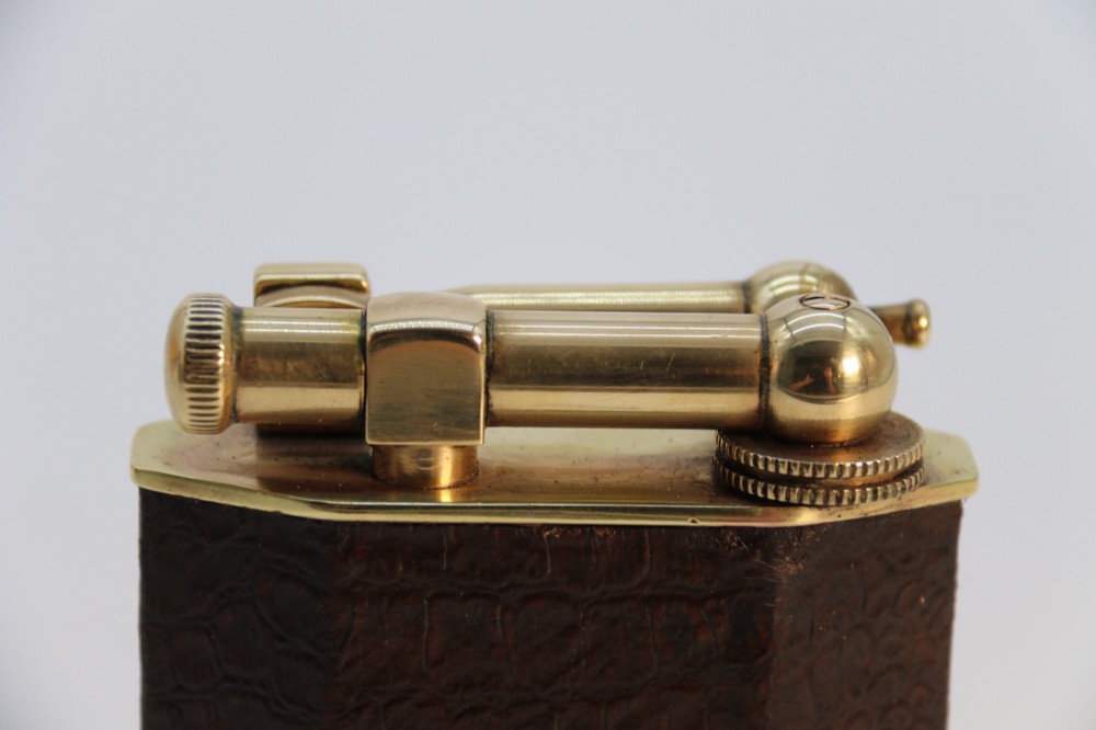 An Art Deco French table lighter featuring a textured brown leather-wrapped faceted body and a polished brass lift-arm ignition mechanism. View X