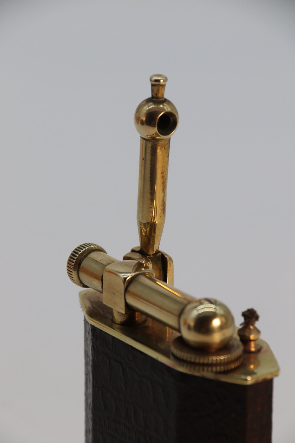 An Art Deco French table lighter featuring a textured brown leather-wrapped faceted body and a polished brass lift-arm ignition mechanism. View XIV