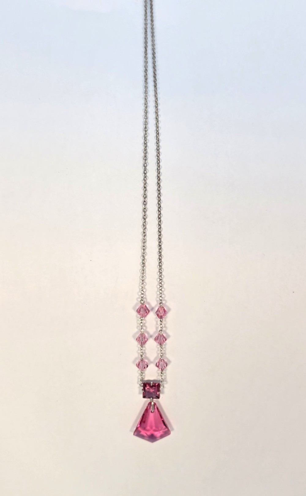 An Art Deco style silver chain necklace featuring faceted pink crystal bicone beads and a geometric triangular crystal pendant drop. View V