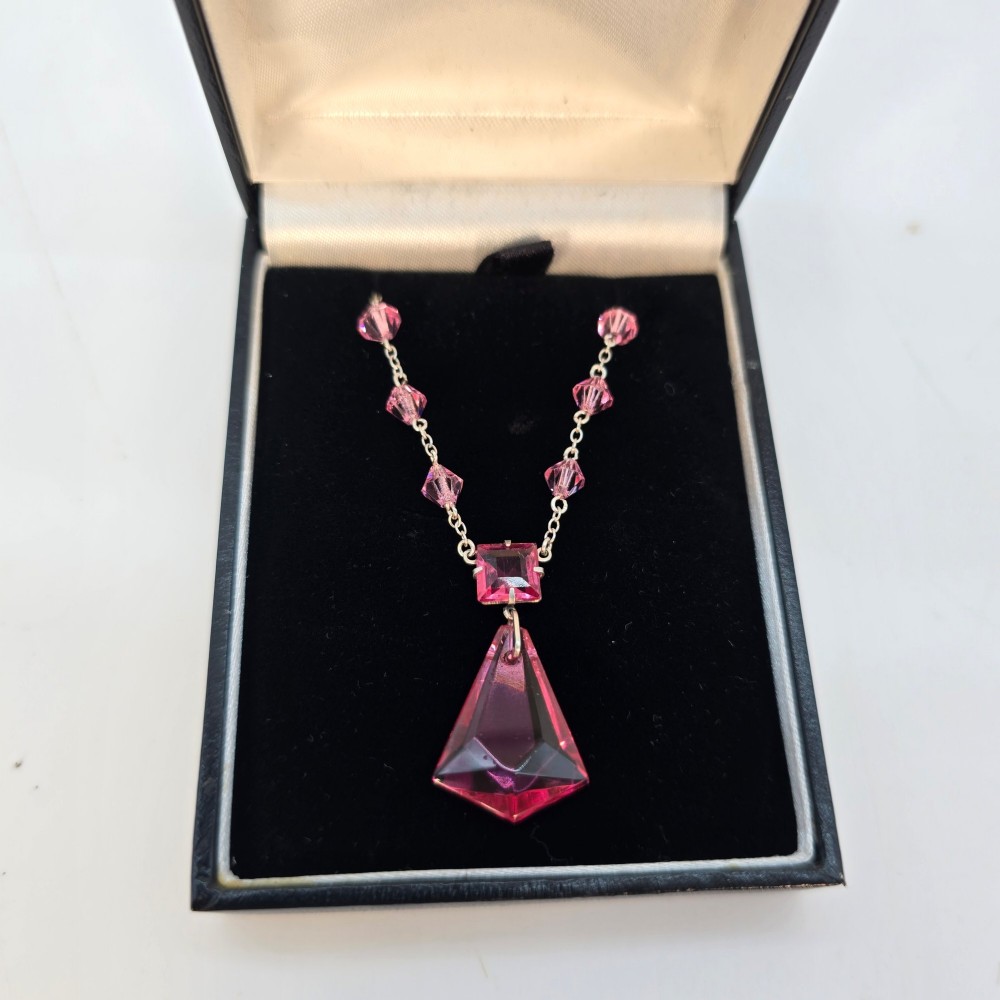 An Art Deco style silver chain necklace featuring faceted pink crystal bicone beads and a geometric triangular crystal pendant drop. View IX
