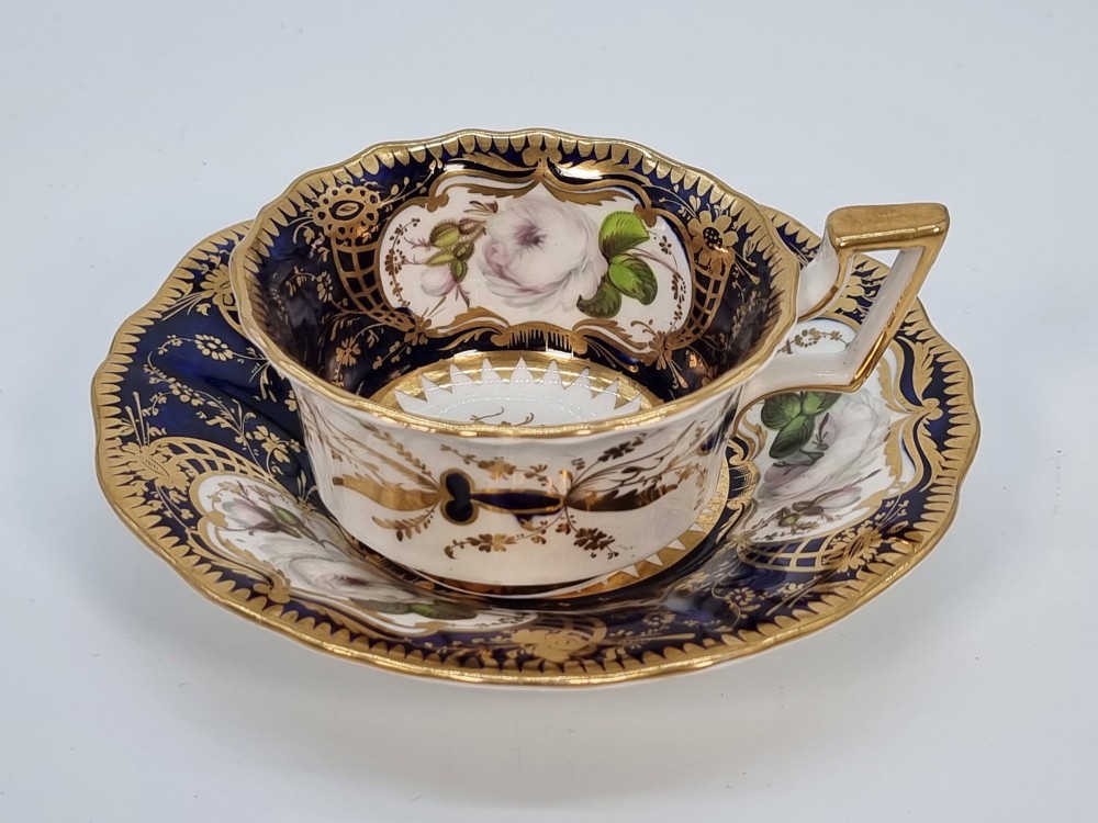 An early nineteenth-century porcelain cabinet trio comprising a teacup, coffee cup, and scalloped saucer decorated with cobalt blue panels, gilt gilding, and hand-painted white rose reserves. View II