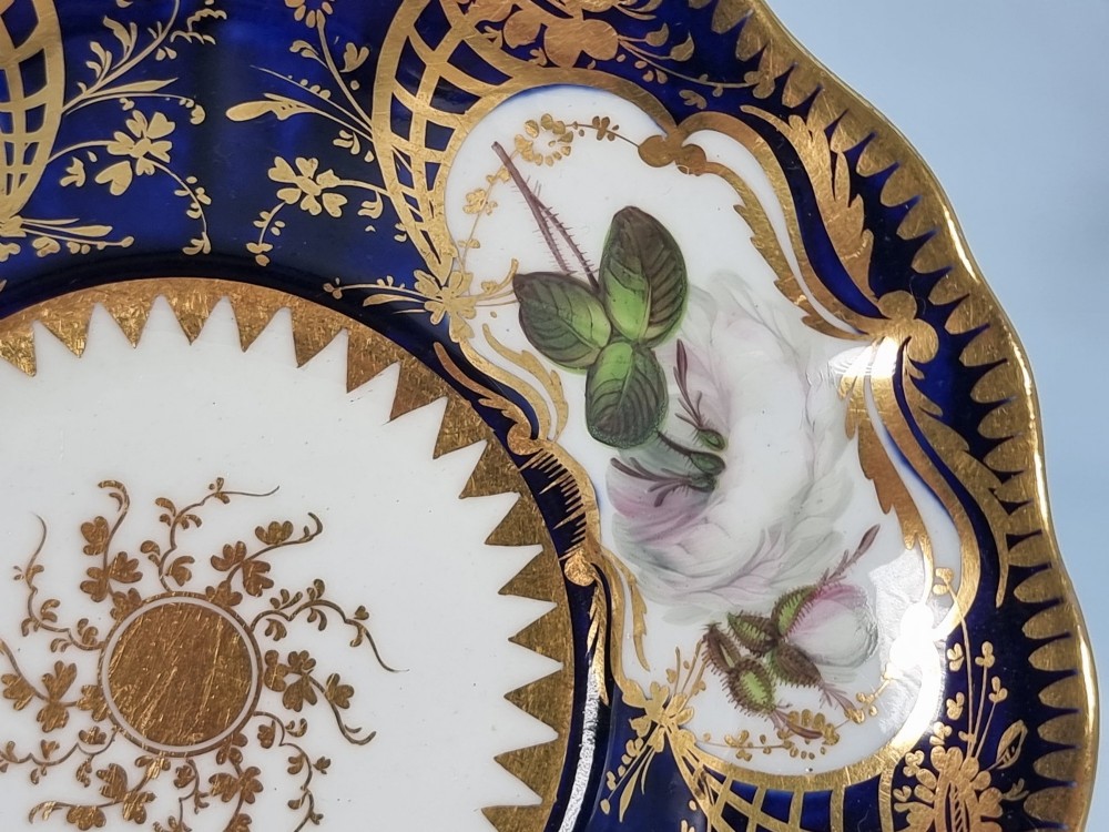 An early nineteenth-century porcelain cabinet trio comprising a teacup, coffee cup, and scalloped saucer decorated with cobalt blue panels, gilt gilding, and hand-painted white rose reserves. View V