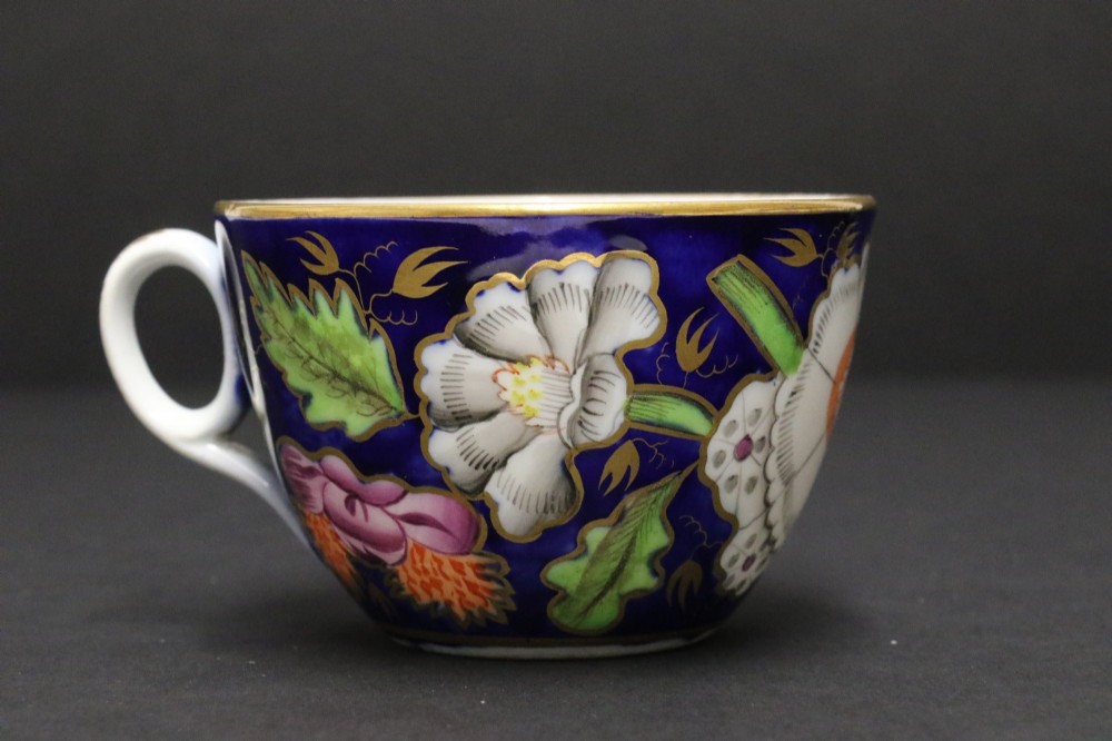 An early 19th-century English Newhall porcelain cabinet trio with a cobalt blue ground, hand-painted botanical flowers, and gilded borders. View II