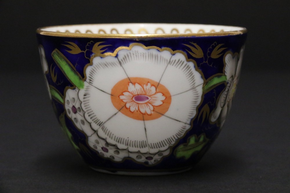An early 19th-century English Newhall porcelain cabinet trio with a cobalt blue ground, hand-painted botanical flowers, and gilded borders. View V