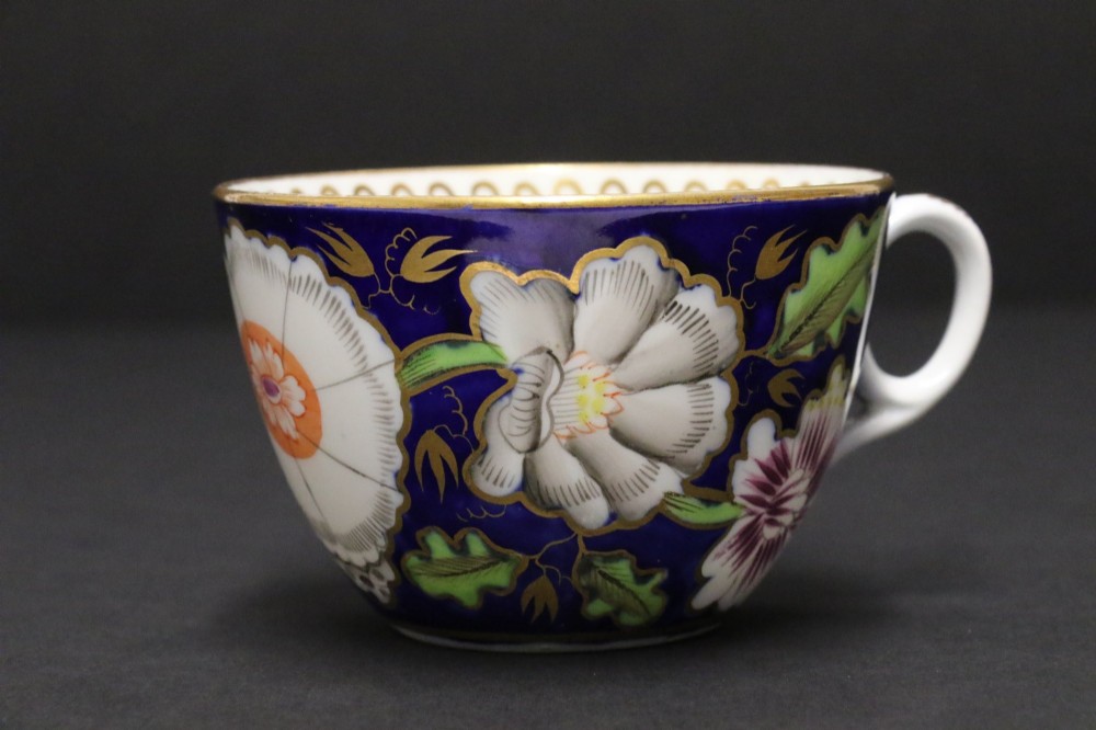 An early 19th-century English Newhall porcelain cabinet trio with a cobalt blue ground, hand-painted botanical flowers, and gilded borders. View VI