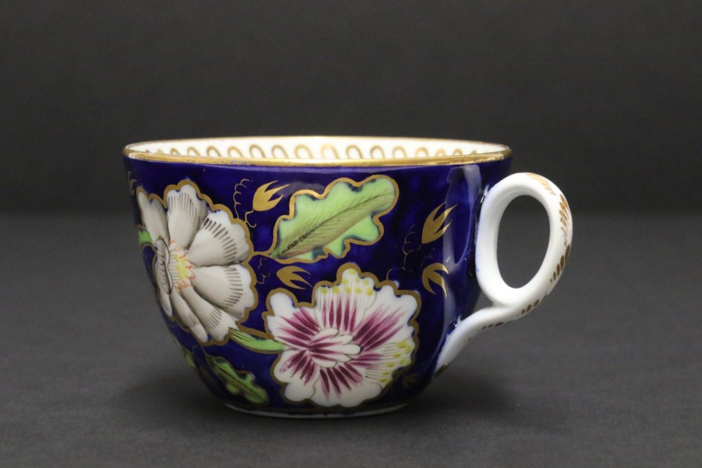 An early 19th-century English Newhall porcelain cabinet trio with a cobalt blue ground, hand-painted botanical flowers, and gilded borders. View VII