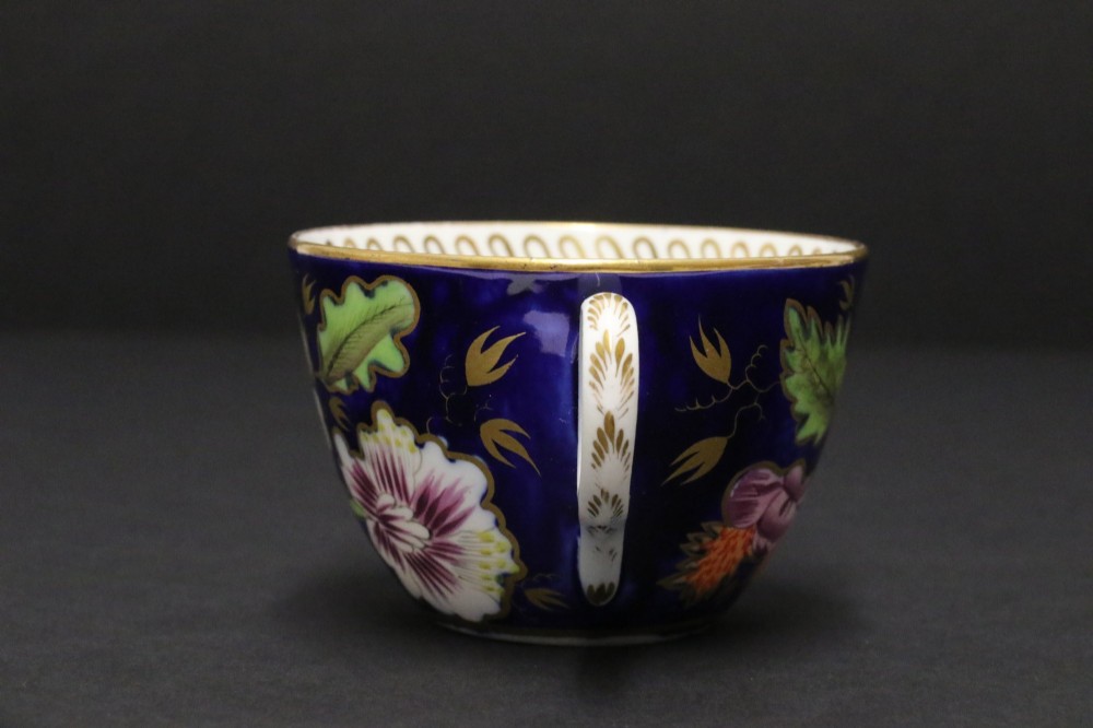 An early 19th-century English Newhall porcelain cabinet trio with a cobalt blue ground, hand-painted botanical flowers, and gilded borders. View VIII