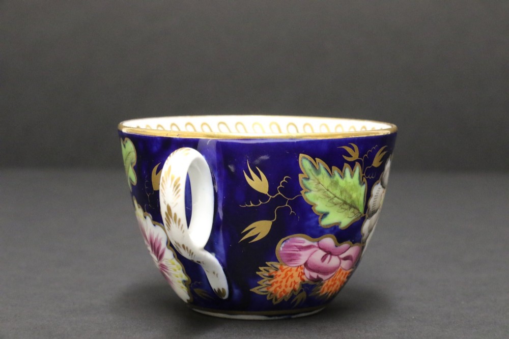 An early 19th-century English Newhall porcelain cabinet trio with a cobalt blue ground, hand-painted botanical flowers, and gilded borders. View IX
