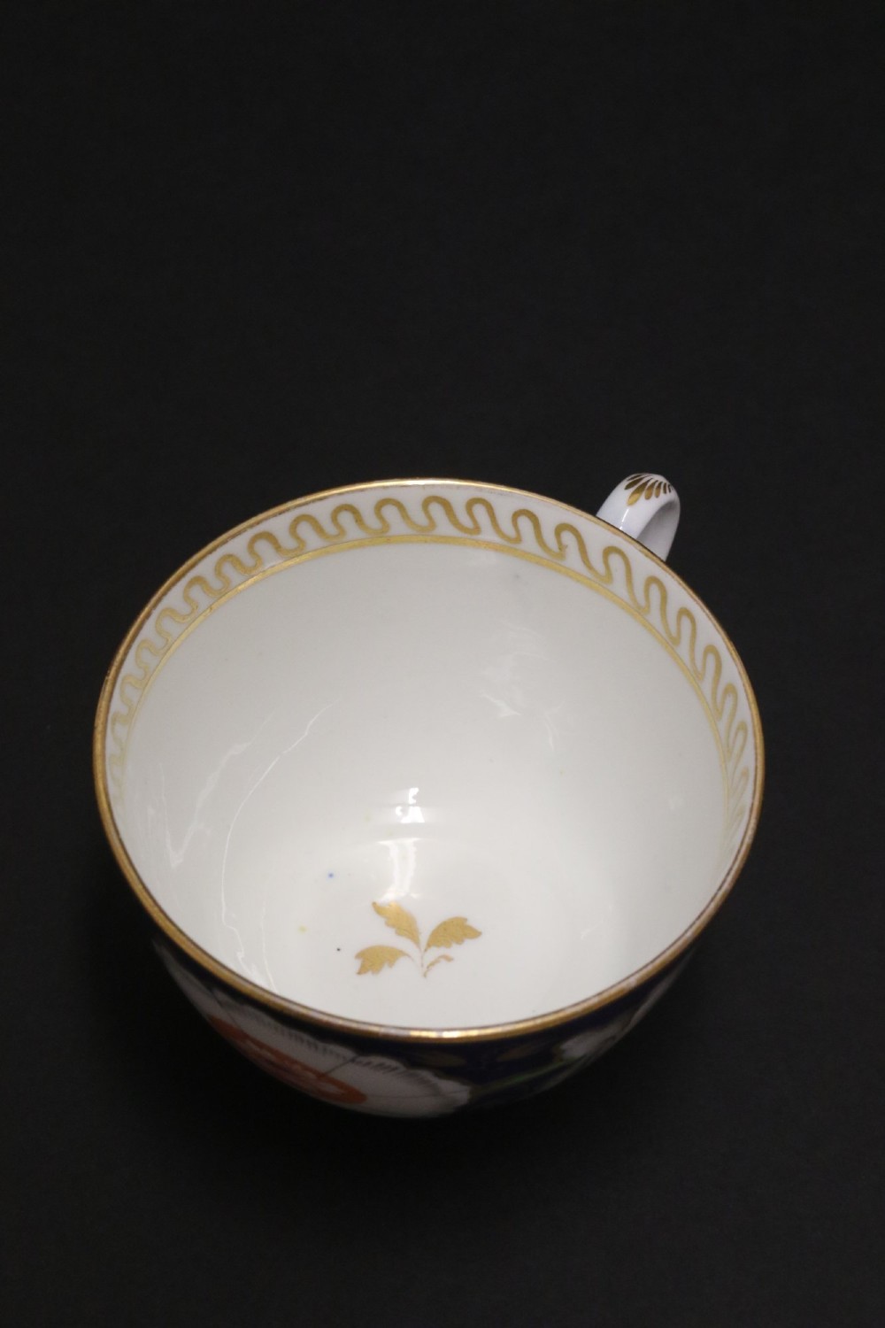 An early 19th-century English Newhall porcelain cabinet trio with a cobalt blue ground, hand-painted botanical flowers, and gilded borders. View X